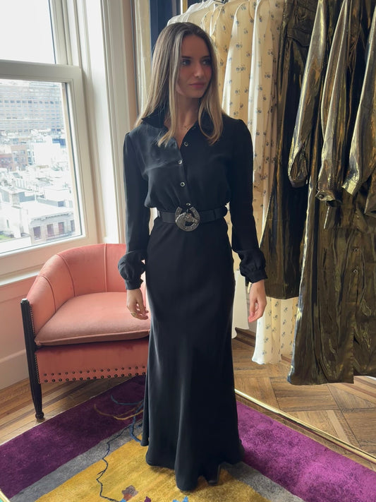 Dahlia maxi dress in Washed Black, belted and standing beside a clothing rack and window