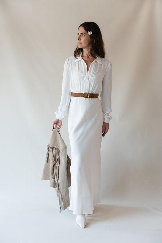 Dahlia maxi dress in Cloud, brown belt at the waist, holding a fringe suede jacket