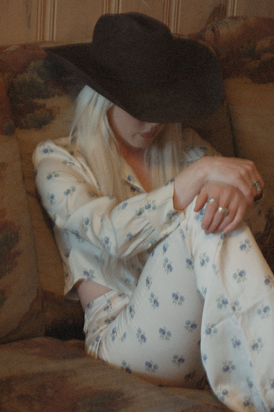 Bridget bell-bottom pants in Kindred Floral, seated with one knee raised, black cowboy hat