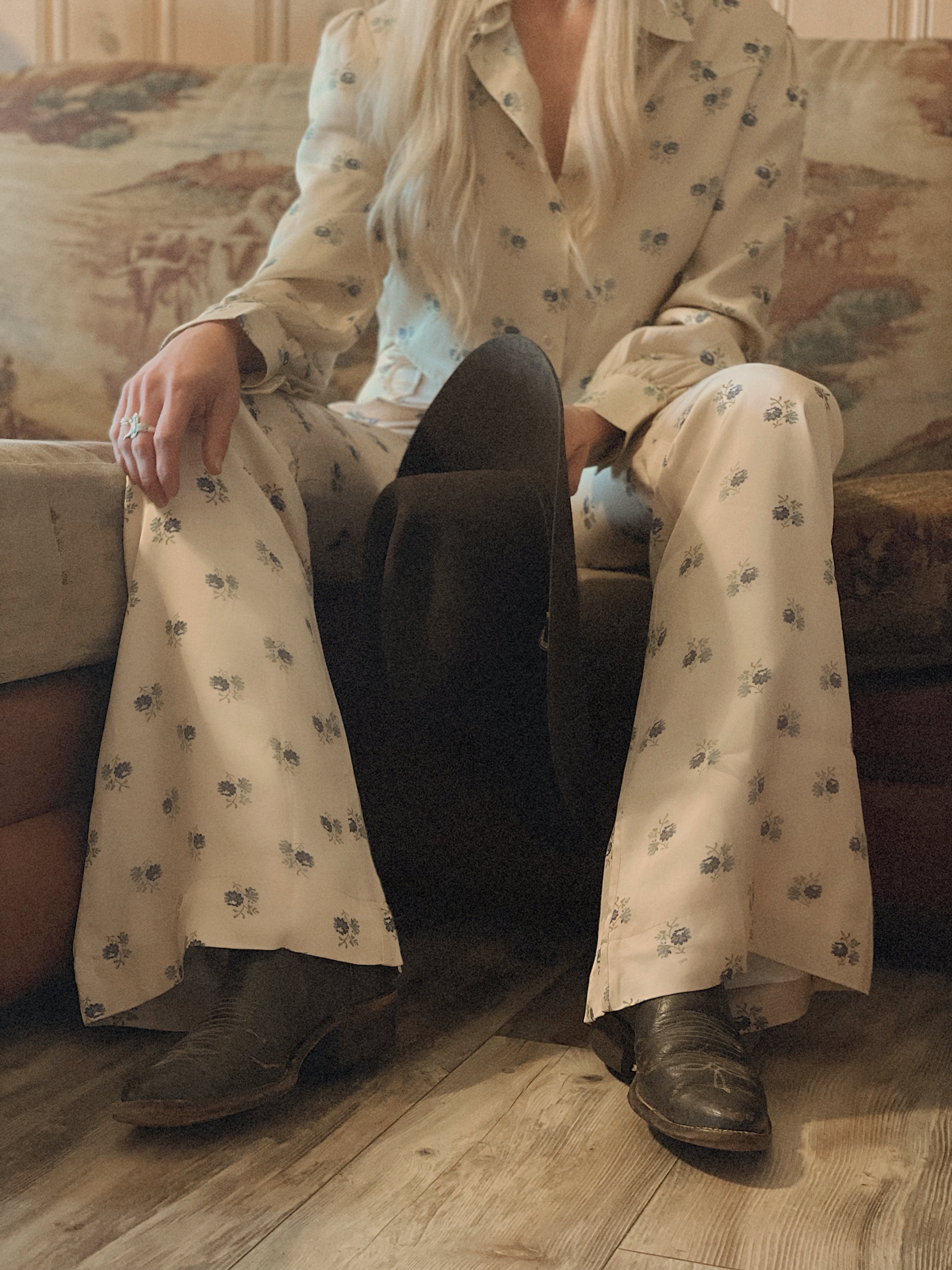 Person wearing a patterned outfit with cowboy boots sitting on a couch.