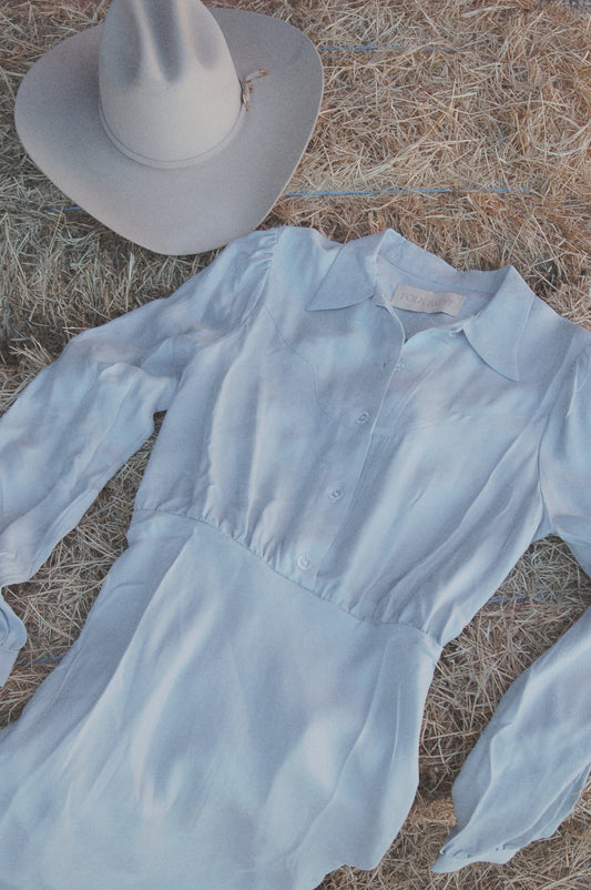 Dahlia maxi dress in Hazy Blue, flat lay on hay beside a cowboy hat