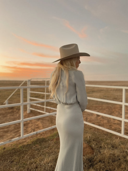 Dahlia maxi dress in Hazy Blue, back view standing at a white pipe fence at dusk