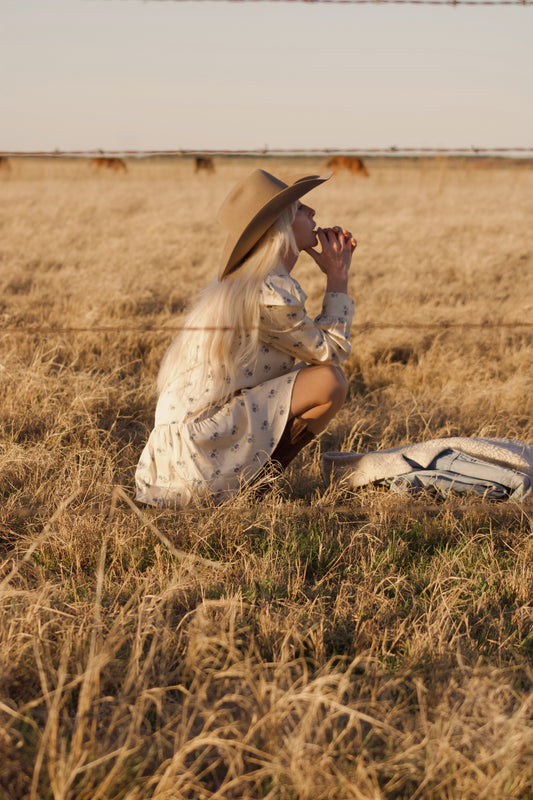 Sienna mini dress in Kindred Floral, crouching in dry grass at golden hour