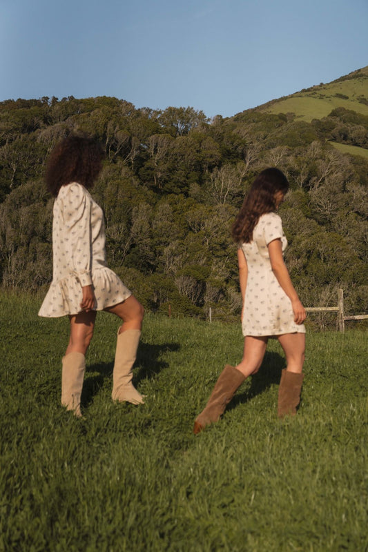 West shirt dress in Kindred Floral, walking through grass beside a ruffle-hem floral dress