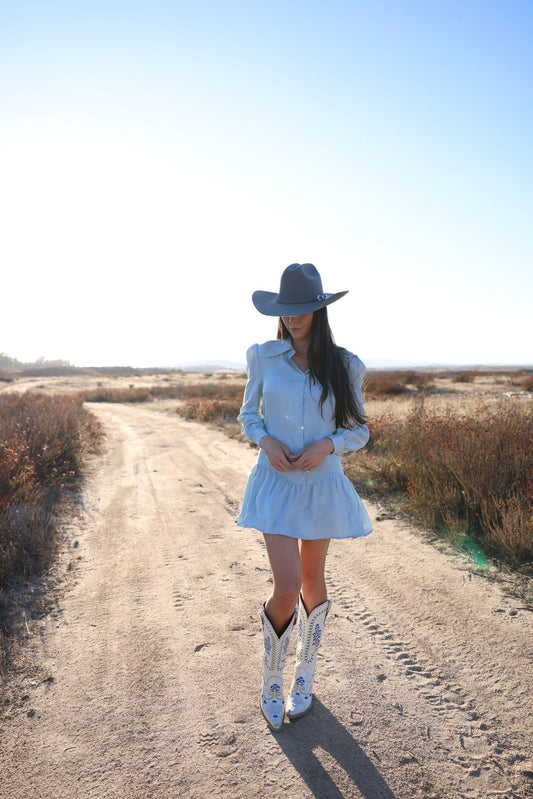 Sienna mini dress in Hazy Blue, front view on a dirt road with a blue cowboy hat