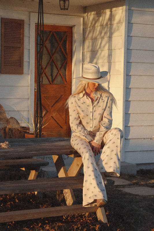 Bridget bell-bottom pants in Kindred Floral, worn with matching blouse on a porch picnic table